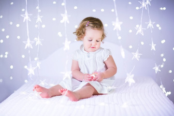 Fototapeta na wymiar Beautiful toddler girl on white bed between Christmas lights