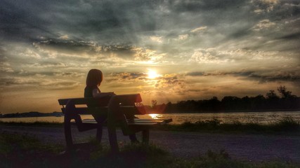 Fototapeta na wymiar Eine Frau sitzt auf einer Bank und genießt den Sonnenuntergang