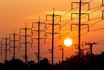 Silhouette high voltage post over orange sunset sky background.