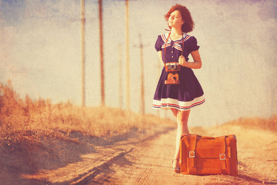 Beautiful brunette girl with suitcase on the countryside road.