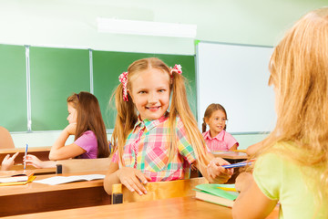 Smiling girls turned to classmate giving pencil