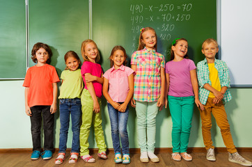 Kids stand in line near the blackboard and smile