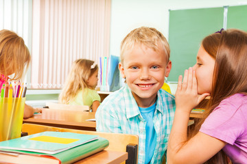 Girl telling secret to smiling boy in classroom