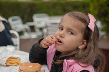 Cute little girl eats hamburger with potato sitting in cafe outd © kemih