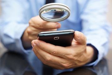 Businessman using mobile smart phone with magnifying glass . Pho