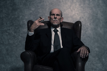 Cigar smoking senior businessman with gray beard wearing dark su