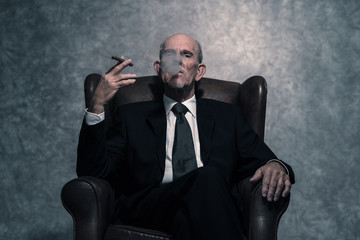 Cigar smoking senior businessman with gray beard wearing dark su