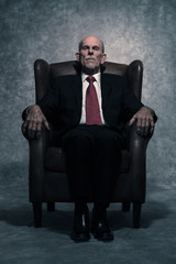 In leather chair sitting senior businessman with gray beard wear