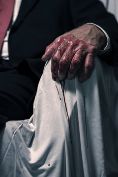 Bloody hand of businessman sitting in white chair.