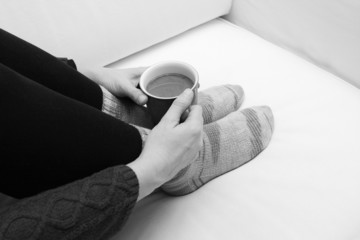 Woman's hands holding a hot beverage, sitting on a couch