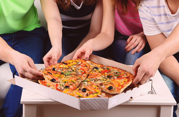 Group of young friends eating pizza in living-room on sofa