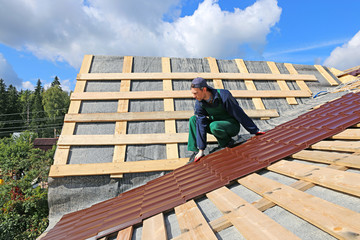 Worker puts the metal tiles on the roof of a wooden house