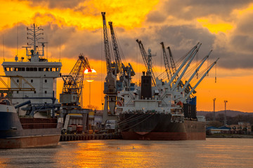 Fototapeta premium Ships and cranes with port warehouse at sunset.