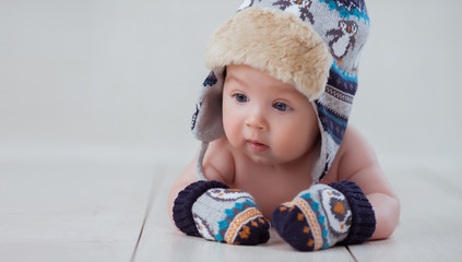 Baby in winter hat and mittens lying on the floor