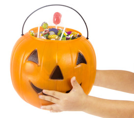 A plastic pumpkin filled with candy and hand of kid