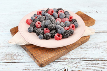 Iced berries on plate, on color wooden background