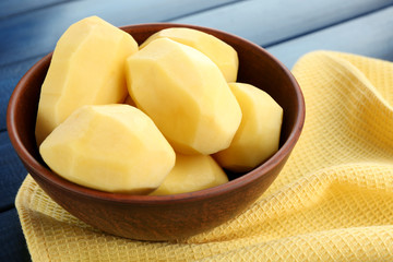 Raw peeled potatoes in bowl  on color wooden background