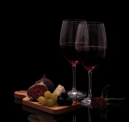 Two glasses red wine with cheese, rose, figs and grapes