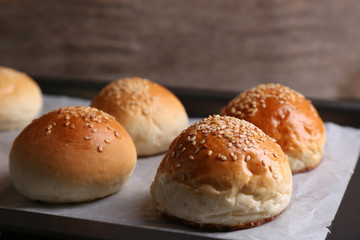 Tasty buns with sesame on oven-tray, on wooden background