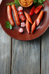 Assortment of tasty thin sausages on plate on wooden background