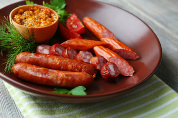 Assortment of tasty thin sausages on plate on wooden background
