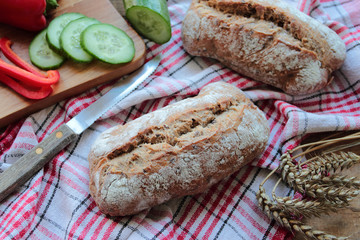Wholemeal bread rolls on a tea towel with fresh vegetables