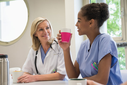 Female doctor and nurse having cup of coffee in hospital canteen