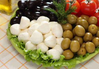 Mozzarella, black and green olives, cherry tomatoes are on green