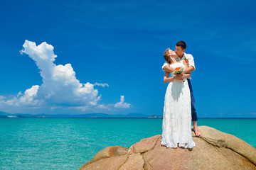 groom and bride standing with bouquet flowers at sea beach