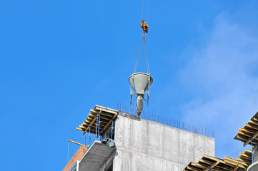 Crane lifting concrete mixer container against blue sky