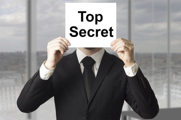 businessman hiding face behind sign top secret
