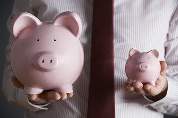 Businessman Holding Large And Small Piggy Bank