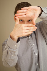 Fototapeta premium Young Caucasian man looks through hands frame, casual studio por