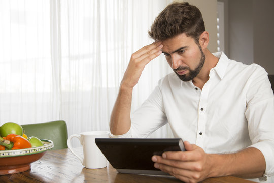 Man seems to be worried while reading information on his tablet