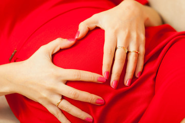 pregnant woman makes heart shape over belly