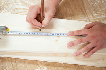 Hands measuring wooden plank with measuring tape and pencil