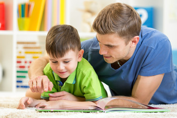 child and his father read a book on floor at home