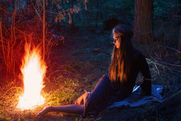 beautiful witch looking at the fire in the forest