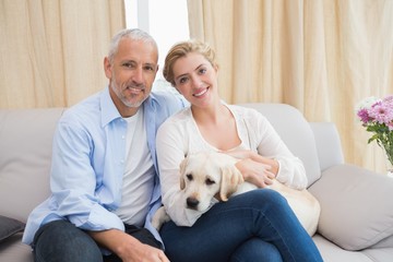 Happy couple cuddling with puppy on sofa