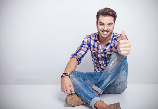 young man smiling while showing the thumbs up gesture.