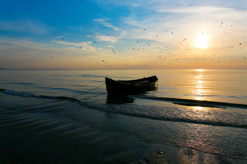 Fisher boat on beach on the sea at sunrise