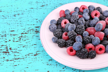 Iced berries on plate, on color wooden background