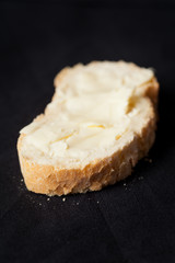 Buttered piece of artisan wheat bread on black background