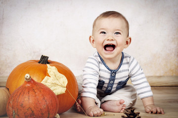 Laughing little baby sitting on the floor with pumpkins