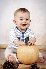 Little baby boy sitting and holding pumpkin