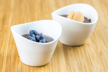 two cups of pudding with blueberries and biscuit on wooden table