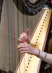 hands of woman strumming the strings of an ancient harp