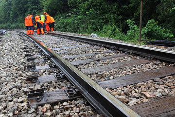 Workers in orange  raincoats repair railroad on rainy day