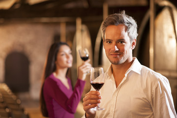Couple tasting a glass of red wine in a traditional cellar surro