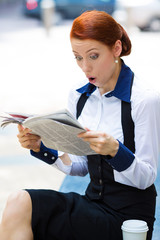 Shocked businesswoman reading newspaper outside office 